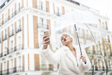 Blonde woman with umbrella texting on smartphone