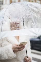 Blonde woman with umbrella texting on smartphone