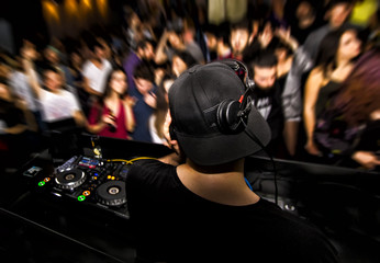 DJ with headphone and dj set at night club party. People at the party are having fun on the...