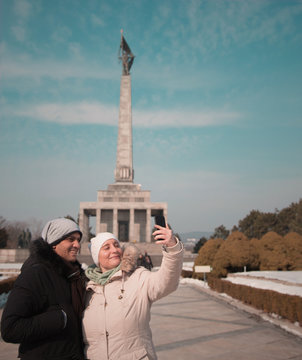 An image of a couple taking 
a selfie againsT one of Bratislava Landmarks; Slavin Statue. Captured in Bratislava, Slovakia.