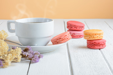 Different types color of macaroons with Cup of hot tea on white wooden background