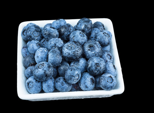 Decorative blueberries with droplets of water. Delicious juicy sweet bilberries in white squered bowl. Isolated on black bacground.