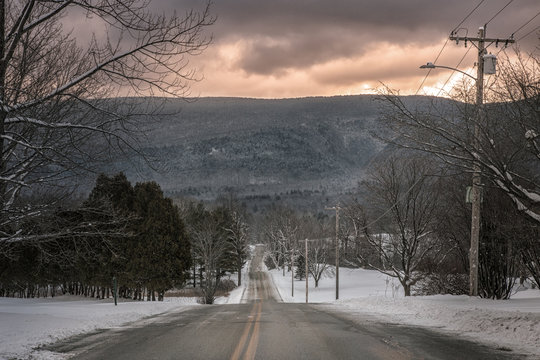 A Long Lonely Winter Road Leading To The Mountains At Dusk.