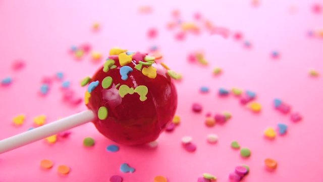 pink round lollipop close-up on pink background. Color glaze in the form of small animal figures is strewed on a red candy. Slow motion