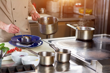 Male chef putting dish in plate. Chef at professional kitchen putting stewing vegetables in steel ring. The process of finishing a dish by chef in restaurant.