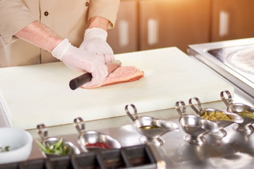 Chef processing meat on board. Male chef hands with knife cutting poultry fillet. Cook preparing meat at work.