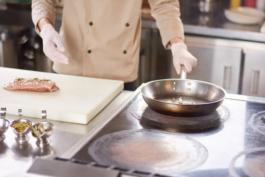 Chef preparing meat at professional kitchen. Cook frying garlic on frying pan. Meat cooking at restaurant kitchen.