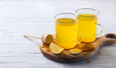 Energy tonic drink with turmeric, ginger, lemon and honey on a wooden board, free space, selective focus