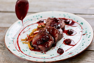 Sliced beef meat with cherry sauce. Veal meat with sweet sauce. Delicious dinner on plate.