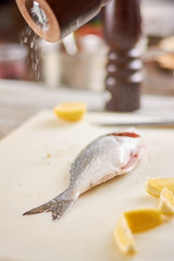 Salt sprinkling on raw fish close up. Process of dorado fish cooking. Raw fish with spices and lemon.