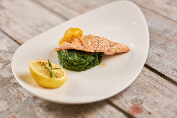Roasted piece of salmon with garnishing. Grilled salmon with lemon and yellow pepper on plate. Tasty dish at restaurant.