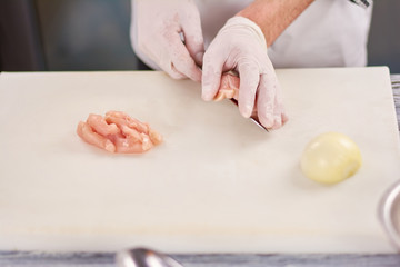 Obraz na płótnie Canvas Chef hands cutting chicken breast. Chef hands chopping raw chicken breast on cutting board. Food preparing, cooking concept.