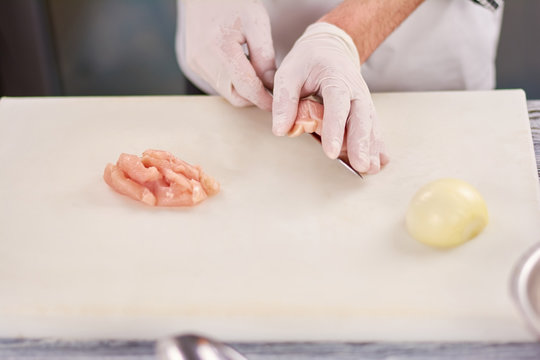 Chef hands cutting chicken breast. Chef hands chopping raw chicken breast on cutting board. Food preparing, cooking concept.