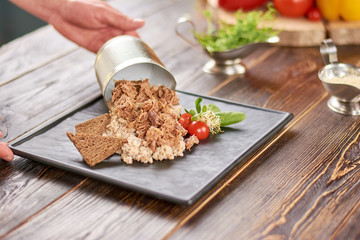 Chef hand pouring out meat from can. Delicious pearl barley with veal meat, cherry tomatoes and bread.