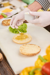 Chef cooking hamburger at professional kitchen. Cook hands putting mustard on bun for burger. Chef at work, kitchen.