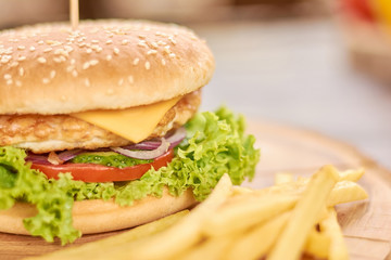 Burger made from fresh vegetables and chicken. Appetizing fresh cheeseburger with french fries close up. Still life with traditional burger and french fries.