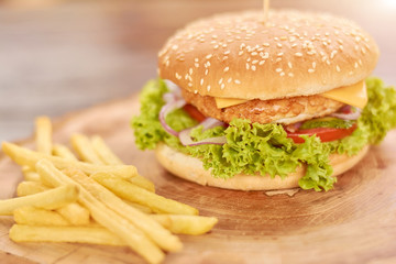 Classic american burger fast food. Hamburger with chicken meat and fresh vegetables. Cheeseburger with french fries on natural wood.