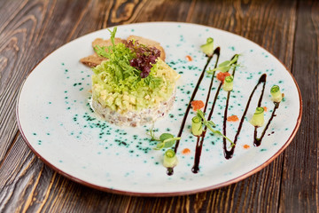 Salad with herring, avocado and toasts. Appetizing dish on plate. Delicious dinner in restaurant.