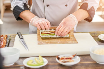 Cook hands making japanese sushi roll. Japanese chef at work preparing delicious sushi roll with eel and avocado. Appetizing japanese food.