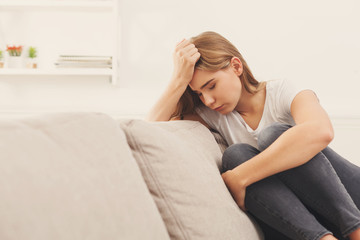 Fototapeta premium Casual blonde girl feeling pain while sitting on the couch