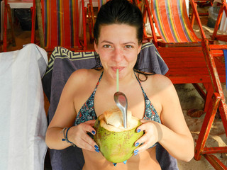 A beautiful and smiling girl is drinking coconut water. It has a special tart to eat the bark inside the coconut walls.