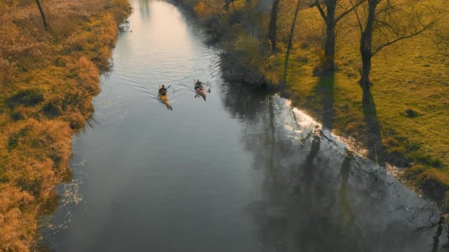 Aerial tracking shot of two kayakers paddling down the river in amazing landscape on a beautiful autumn sunny day.
