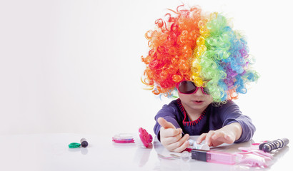 Cute little child girl with colorful hair having fun and doing makeup. Humorous image. Happy childhood, beauty, joy concept.