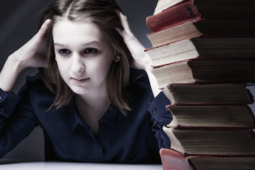 Young depressed female student with books as symbol of heavy and boring education. (Science,...