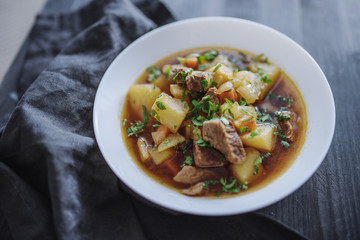 Irish beef stew with fresh parsley on a dark wooden background in natural light