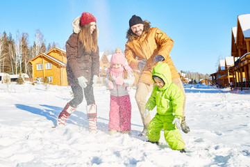 Young Caucasian couple and their little kids playing with snow and smiling happily on beautiful...