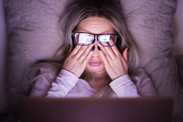 Sleepy young caucasian woman in glasses rubbing her eyes, feels tired after working on a laptop,...