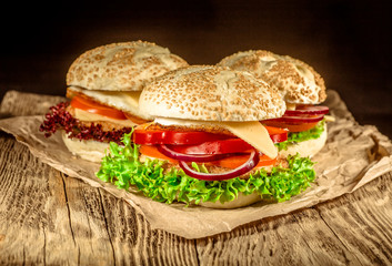 Close-up of delicious fresh home made burger with lettuce, cheese, onion and tomato on a rustic wooden plank on a dark background