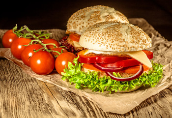 Close-up of delicious fresh home made burger with lettuce, cheese, onion and tomato on a rustic wooden plank on a dark background