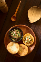 Traditional Chilean Sopaipilla fried pastries made of a bread-like leavened dough, served with a bowl of Chilean pebre salsa on the side, photographed overhead on dark wood with natural light