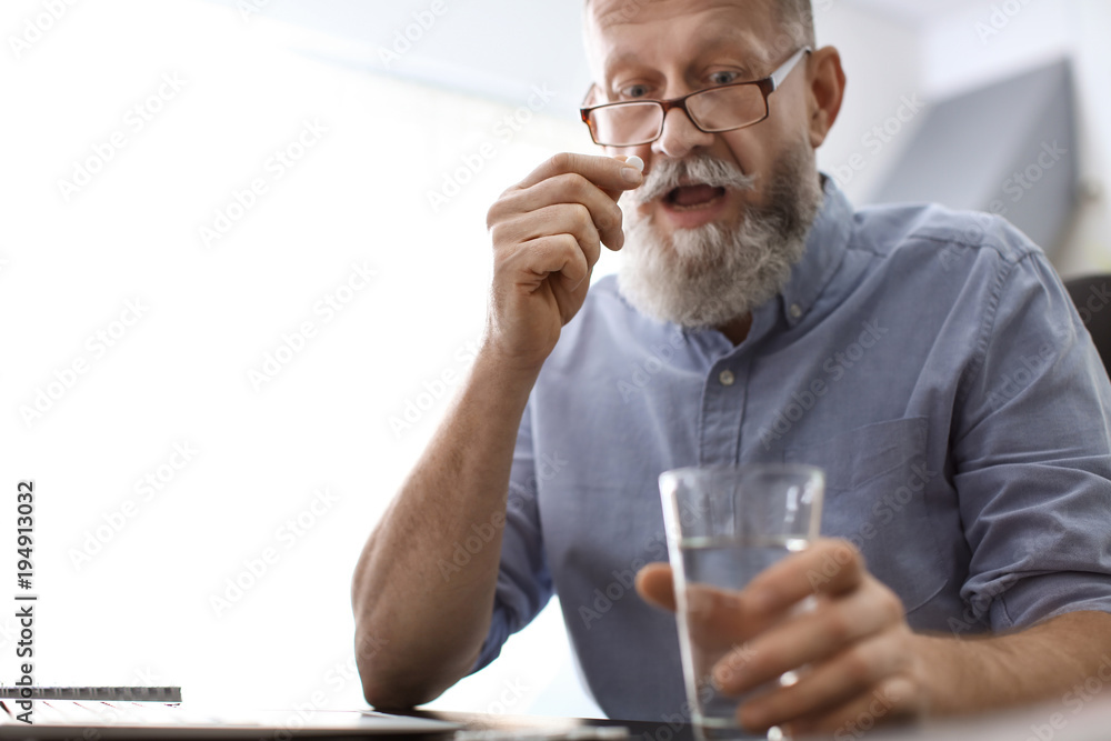 Canvas Prints Senior man taking pill at workplace