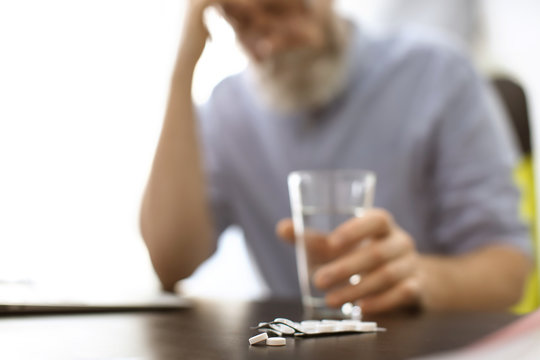 Senior man with pills and glass of water at workplace