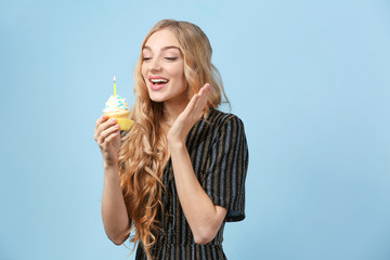 Happy young woman with birthday cupcake on color background
