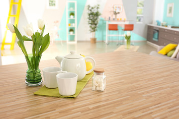 Wooden table with cups and teapot on kitchen