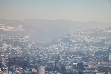 Aerial view of Sarajevo during a sunny winter afternoon, covered in snow. The historical center with its mosques and minarets can be seen in background