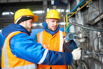 Group of bearded technicians wearing uniform and hardhats gathered together at spacious production...