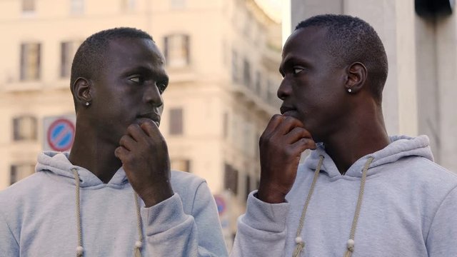 young African black man is mirrored on a shop window in the street