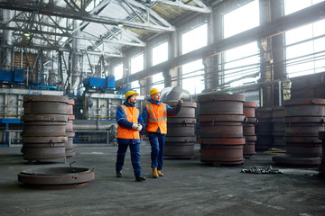 Bearded young worker wearing reflective vest and hardhat showing results of accomplished work to...
