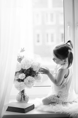 A little girl is sitting on the windowsill. A bouquet of flowers