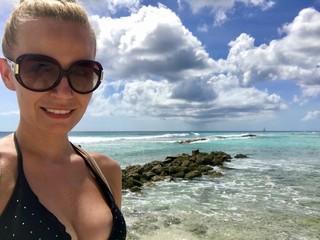 Beautiful happy smiling blonde female model in Barbados wearing a black bikini at a untouched beach...