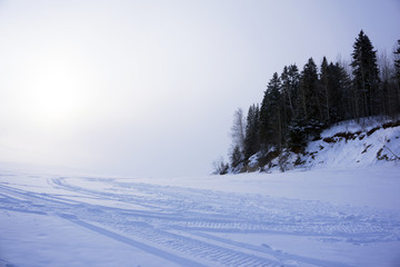 winter road (frozen river with a highly wooded shore) with traces of snowmobiles, with a horizon,...