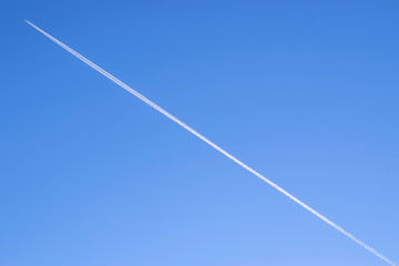 blue background of the sky with a flying plane on it with a white Condensation trail contrail behind it on the entire sky diagonally