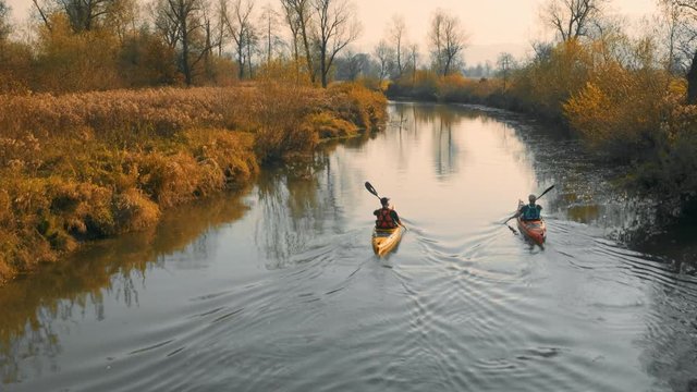 Aerial tracking shot of two kayakers paddling up the river on amazing beautiful autumn sunny day.
