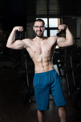 Fototapeta na wymiar Muscular Geek Man Flexing Muscles In Gym