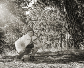 Funny woman crouching in the woods wearing a dress carrying a shotgun