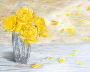 Beautiful yellow roses in a stone vase against a soft blue and yellow wooden background with blowing petals